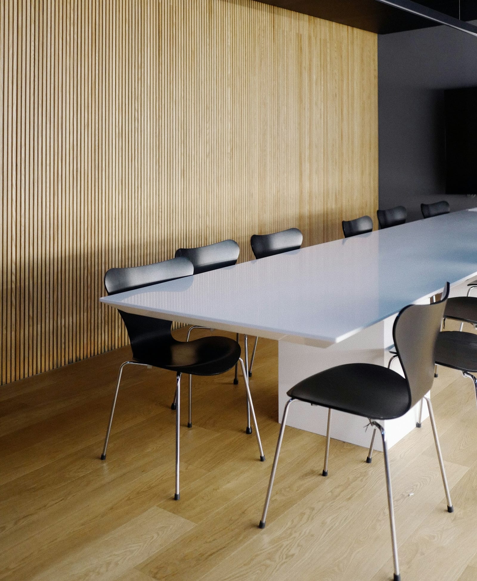 Empty conference room with a long white table and dark chairs by tall windows.